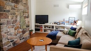 Ein Wohnzimmer mit Steinkamin, Flachbildfernseher, beiges Sofa und Couchtisch aus Holz.