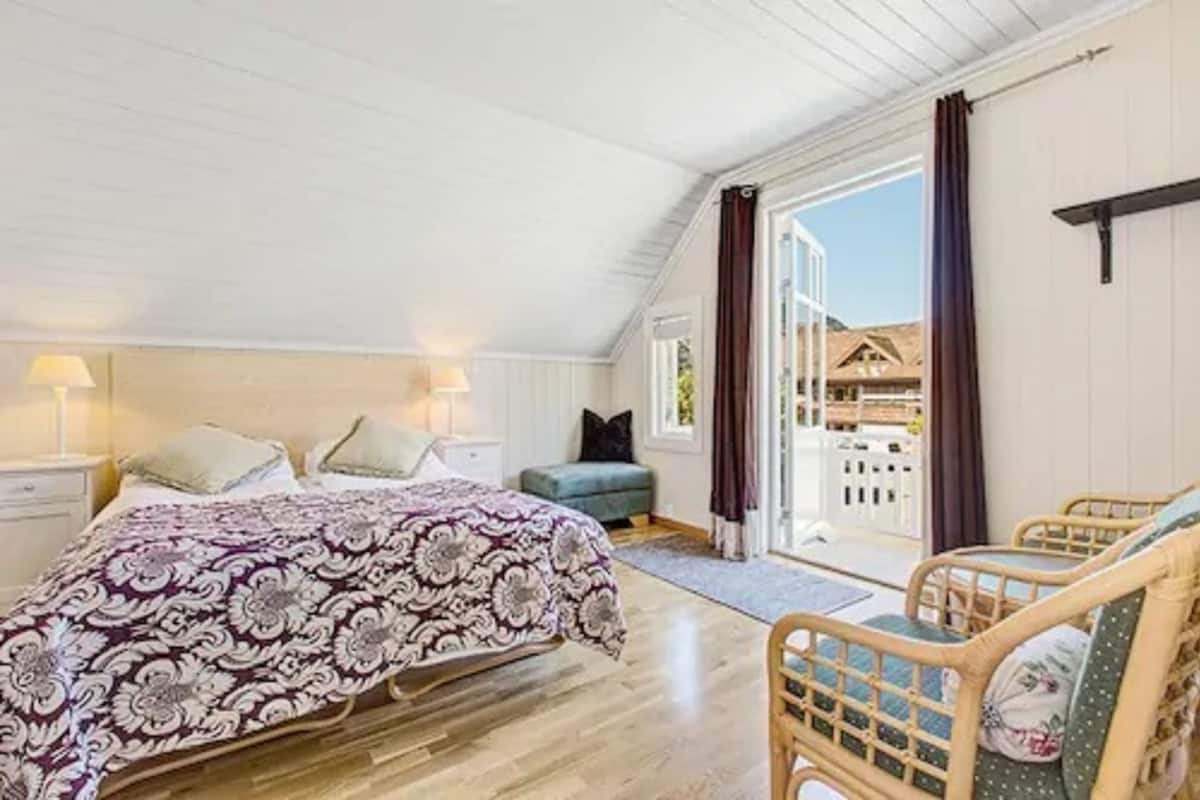A bedroom with a large bed, a nightstand, a chair, and a view of the outside.