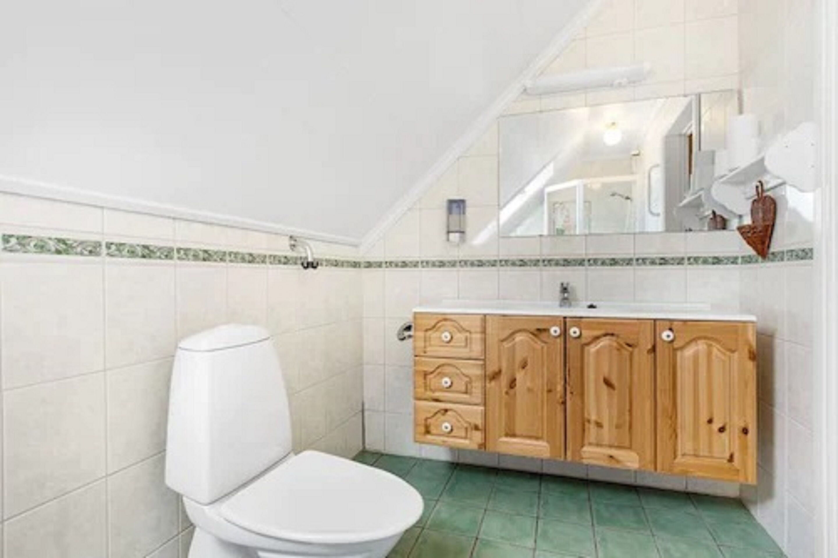 Un baño con inodoro blanco, muebles de madera y piso con baldosas verdes.