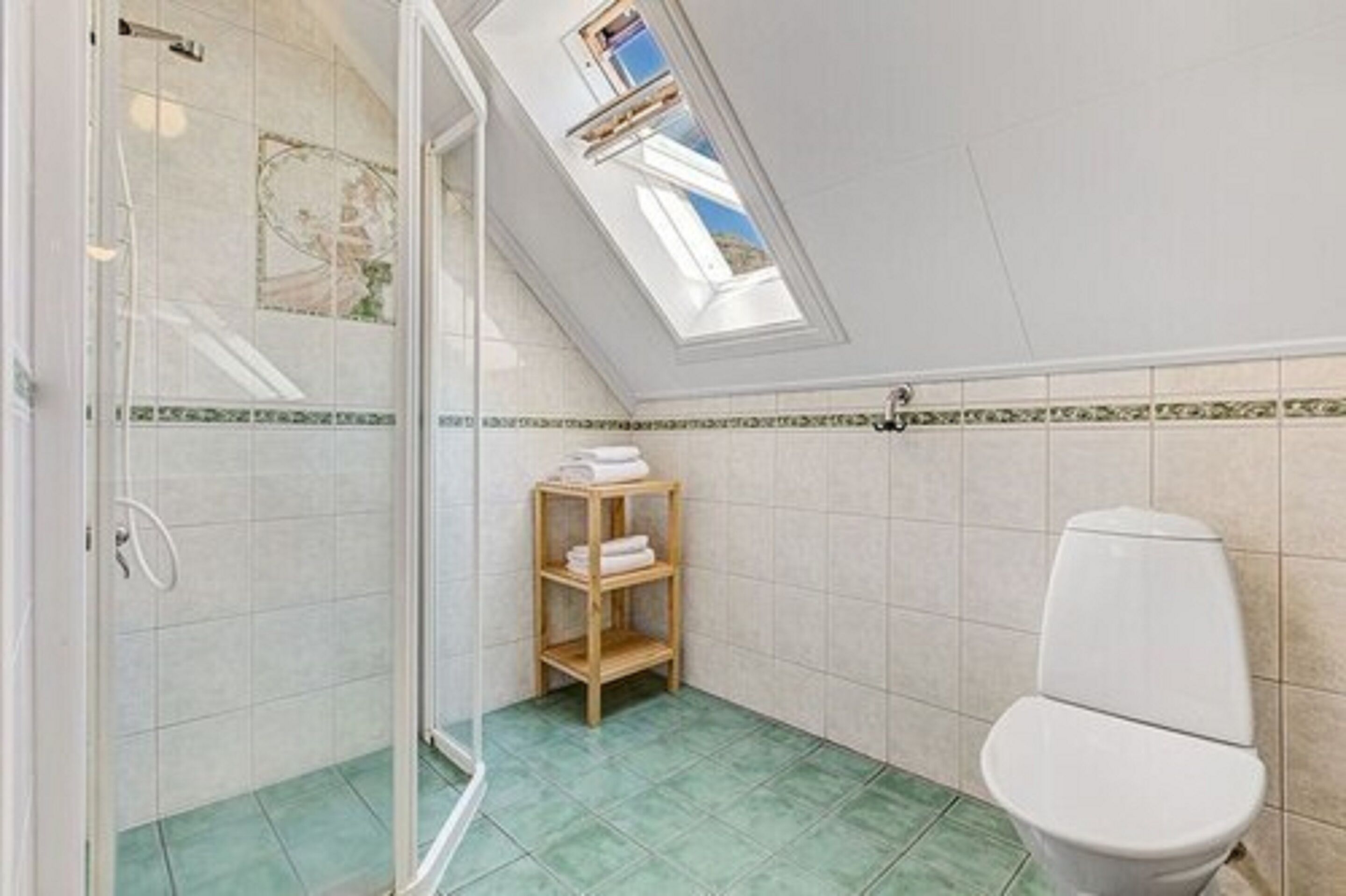 Un baño con tragaluz, ducha, inodoro y estante con toallas.