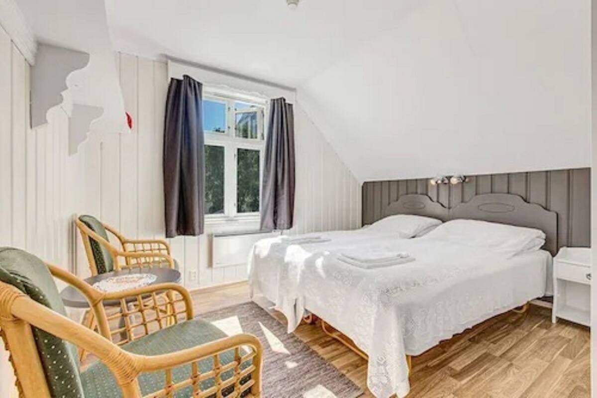 A bedroom with a bed, two chairs, a window with curtains, and a nightstand.