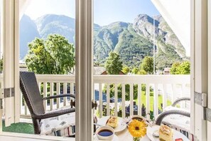 Ein Balkon mit Korbstuhl, Tisch mit Speisen und Getränken sowie Bergblick.