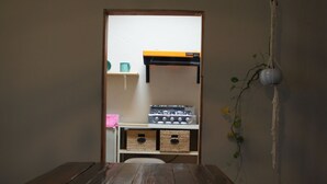 Une table en bois dans une pièce où l’on aperçoit une cuisine par une porte ouverte.