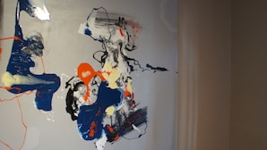 Un grand tableau abstrait accroché au mur, une chaise en bois avec un pot de plante, et un mur uni.