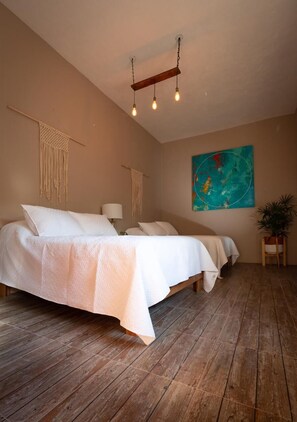 A bedroom with a large bed, wooden flooring, and a hanging light fixture. - Casa Isaki (San Pedro Cholula)