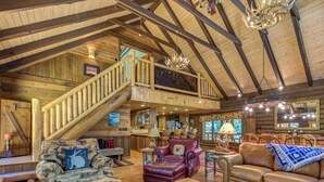 A spacious log cabin interior with a high ceiling, wooden staircase, leather sofas, and a dining area. - Black Bear Lodge by Vtrips (Cosby)