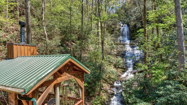 A wooden cabin with a green roof overlooking a waterfall in a forest. - Black Bear Lodge by Vtrips (Cosby)