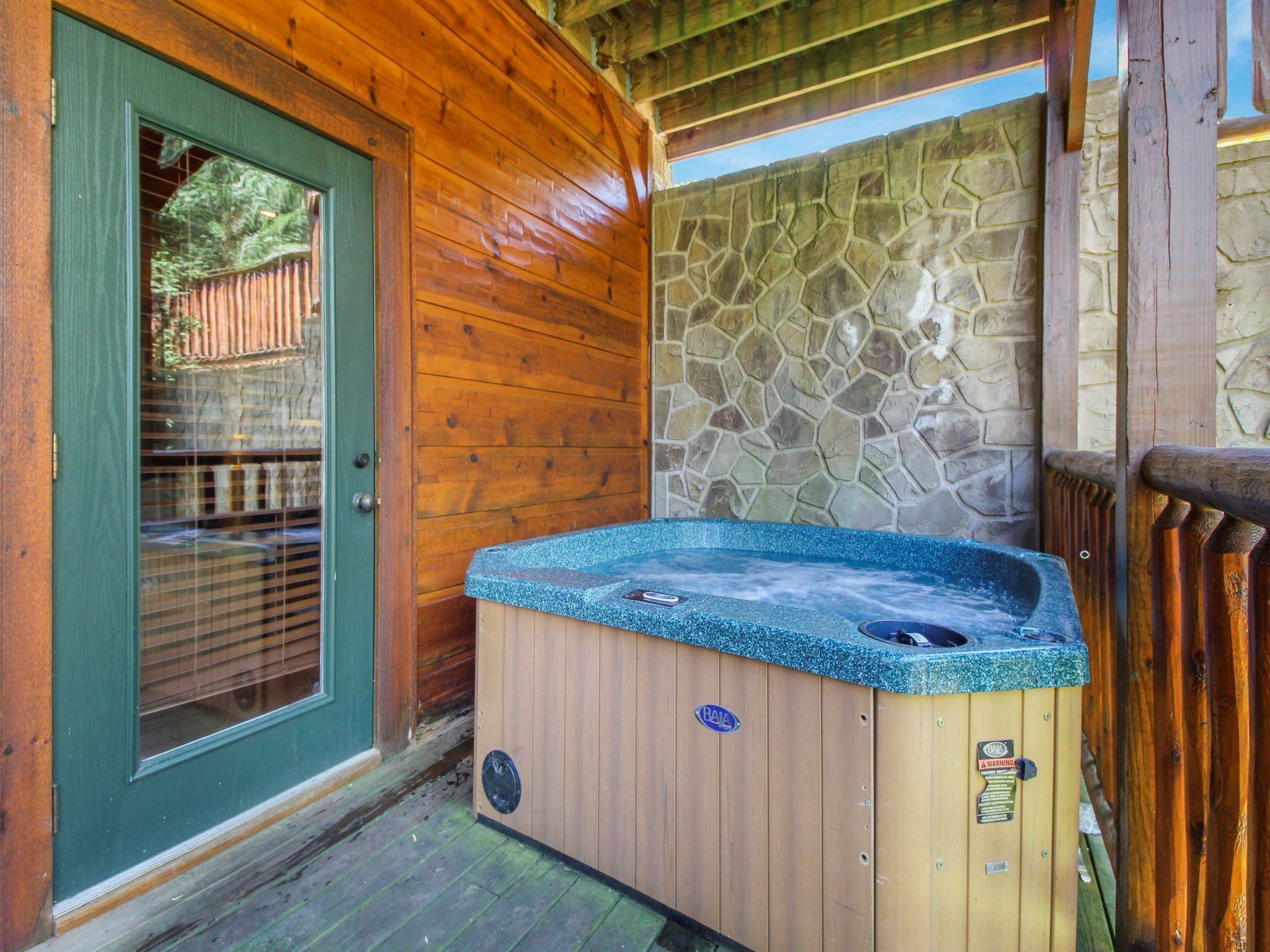 A wooden cabin with a stone wall, a wooden door, and a hot tub.