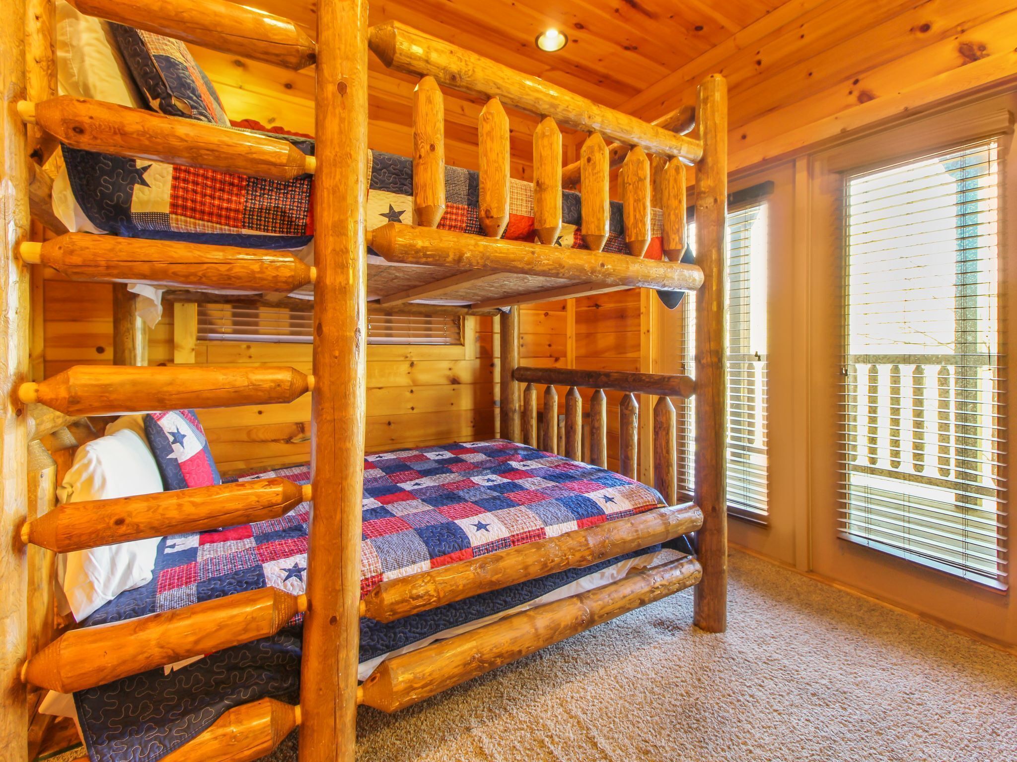 A bunk bed with a quilted bedspread, wooden railings, and a window with blinds.