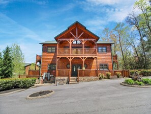 Une cabane en rondins à deux étages, dotée d’un balcon, de fondations en pierre et d’une cour avant bien entretenue.