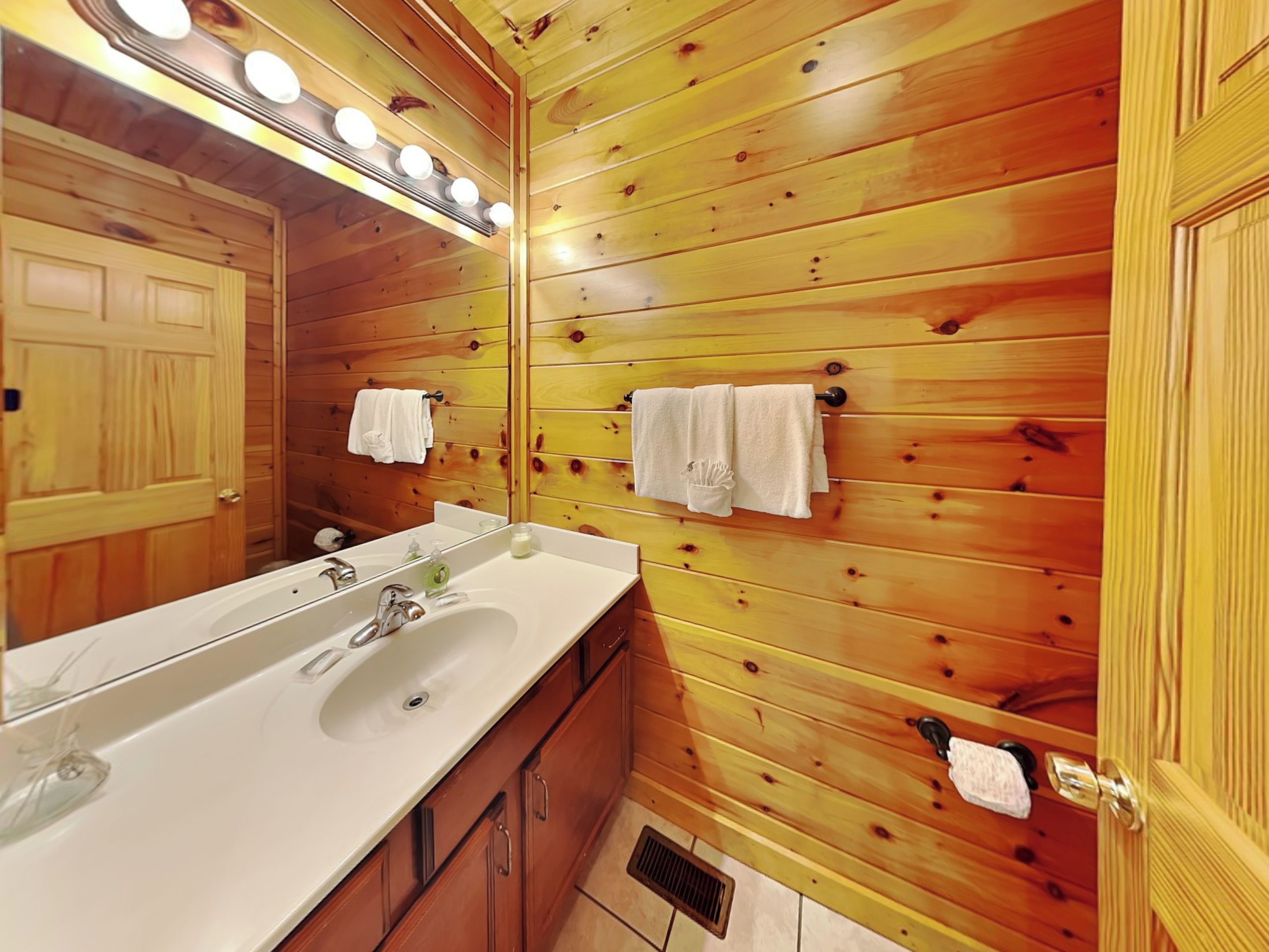Un baño con paneles de madera, un espejo grande, dos lavamanos y toallas colgadas en la pared.