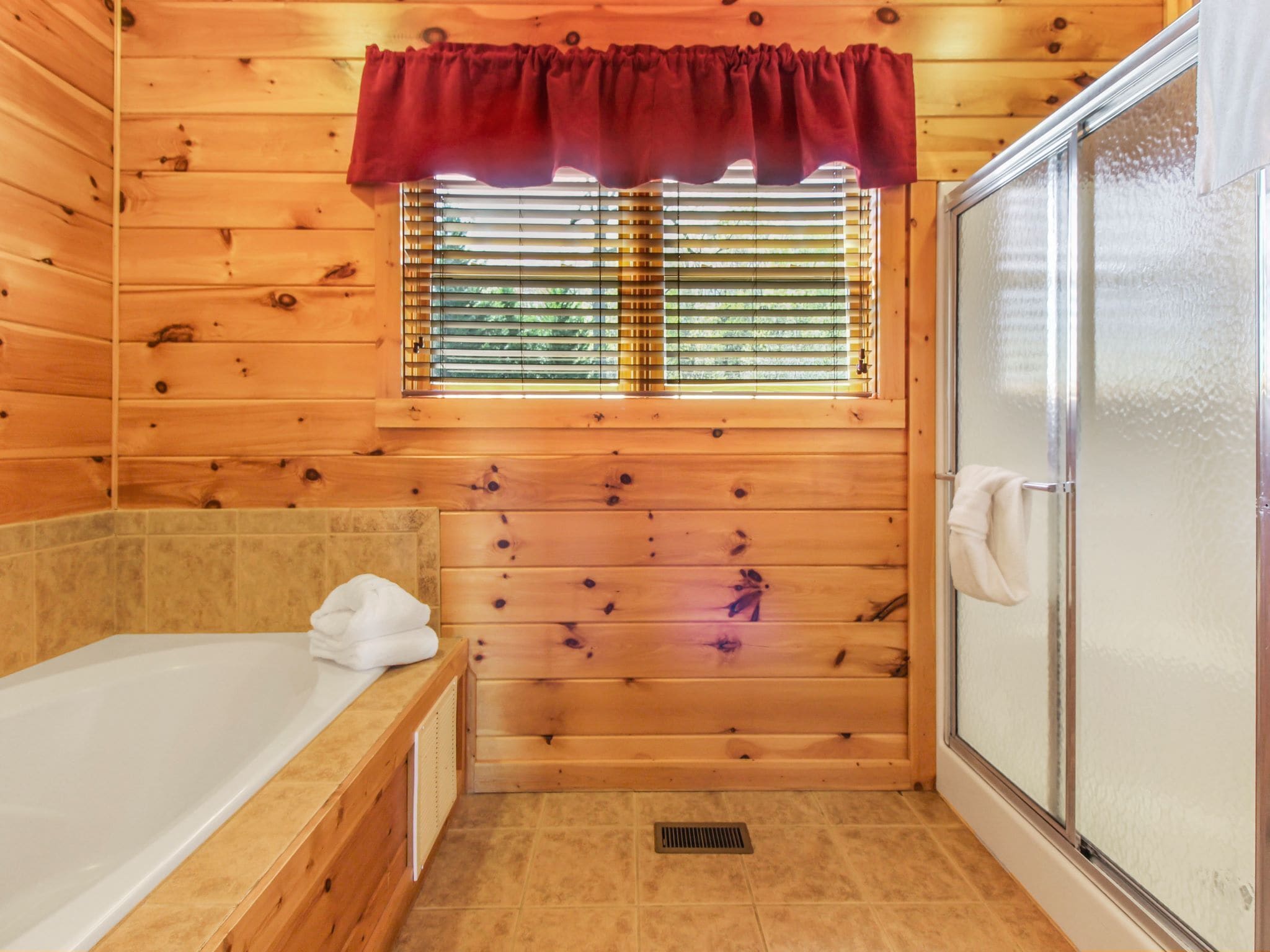 Un baño de cabaña de madera con bañera, una ventana con persianas y zona de ducha.