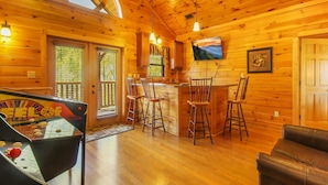 A wooden cabin interior with a bar area, wooden floors, and a large window. - Big Sky Lodge II by Jackson Mountain Rentals (Gatlinburg)