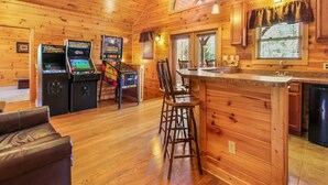 A wooden cabin interior with a bar area, arcade games, and a dining space. - Big Sky Lodge II by Jackson Mountain Rentals (Gatlinburg)