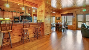A wooden cabin interior with a kitchen area, dining table, and bar stools. - Big Sky Lodge II by Jackson Mountain Rentals (Gatlinburg)