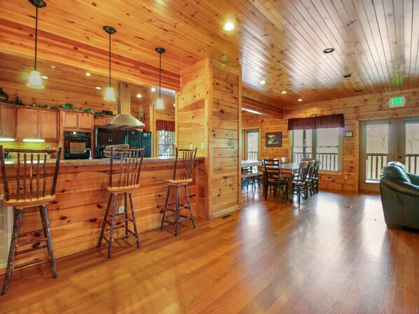 A wooden cabin interior with a kitchen area, dining table, and bar stools. - Big Sky Lodge II by Jackson Mountain Rentals (Gatlinburg)