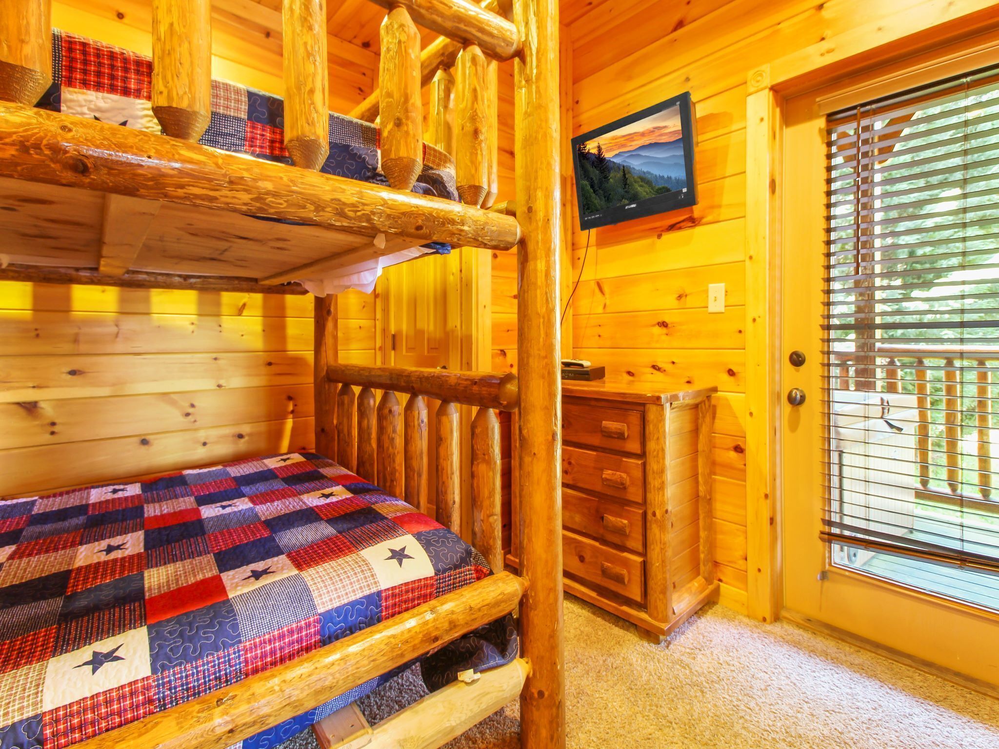 A cozy cabin room with a bunk bed, a wooden dresser, and a television mounted on the wall.
