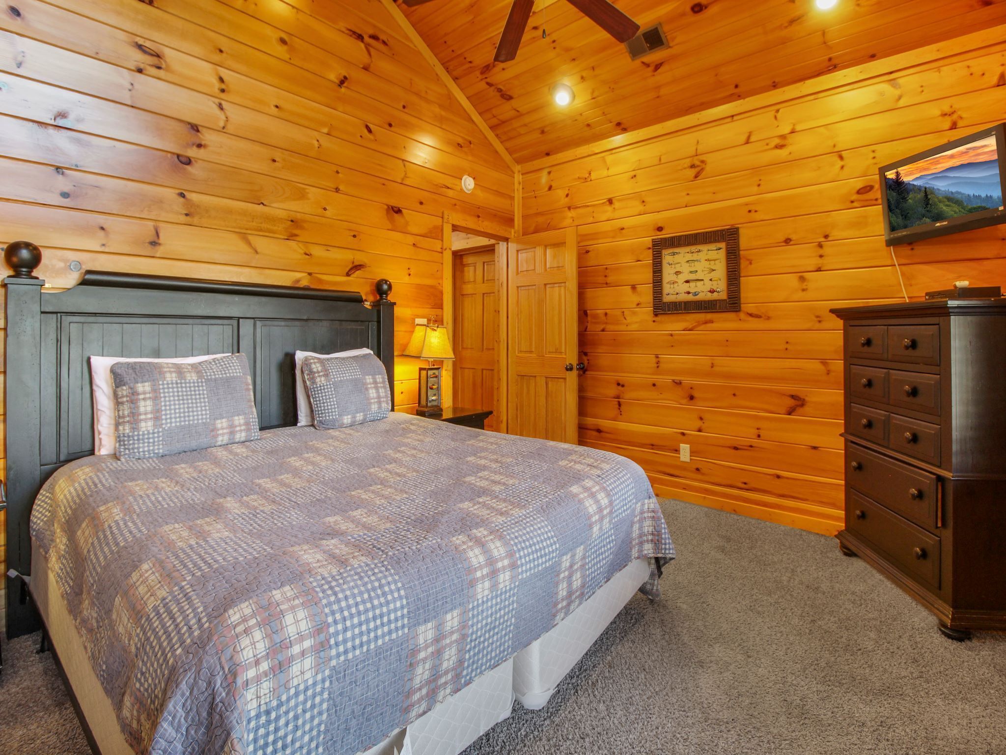 Un dormitorio tipo cabaña de madera con cama, cómoda y televisor de pared mostrando una vista panorámica.