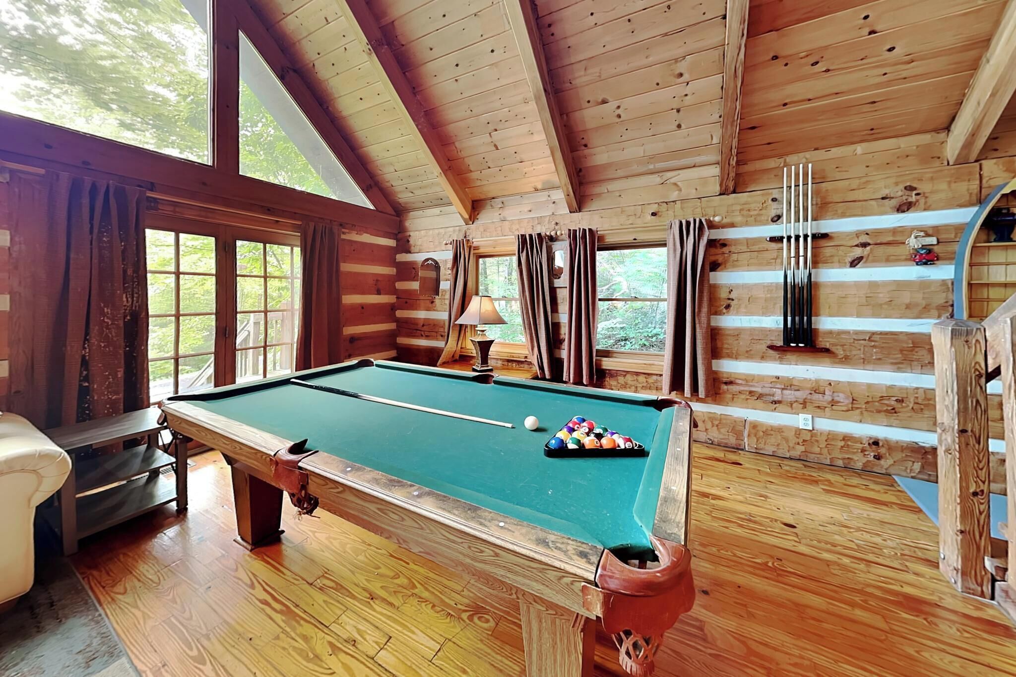 A wooden cabin with a pool table, a sofa, and a billiards rack.