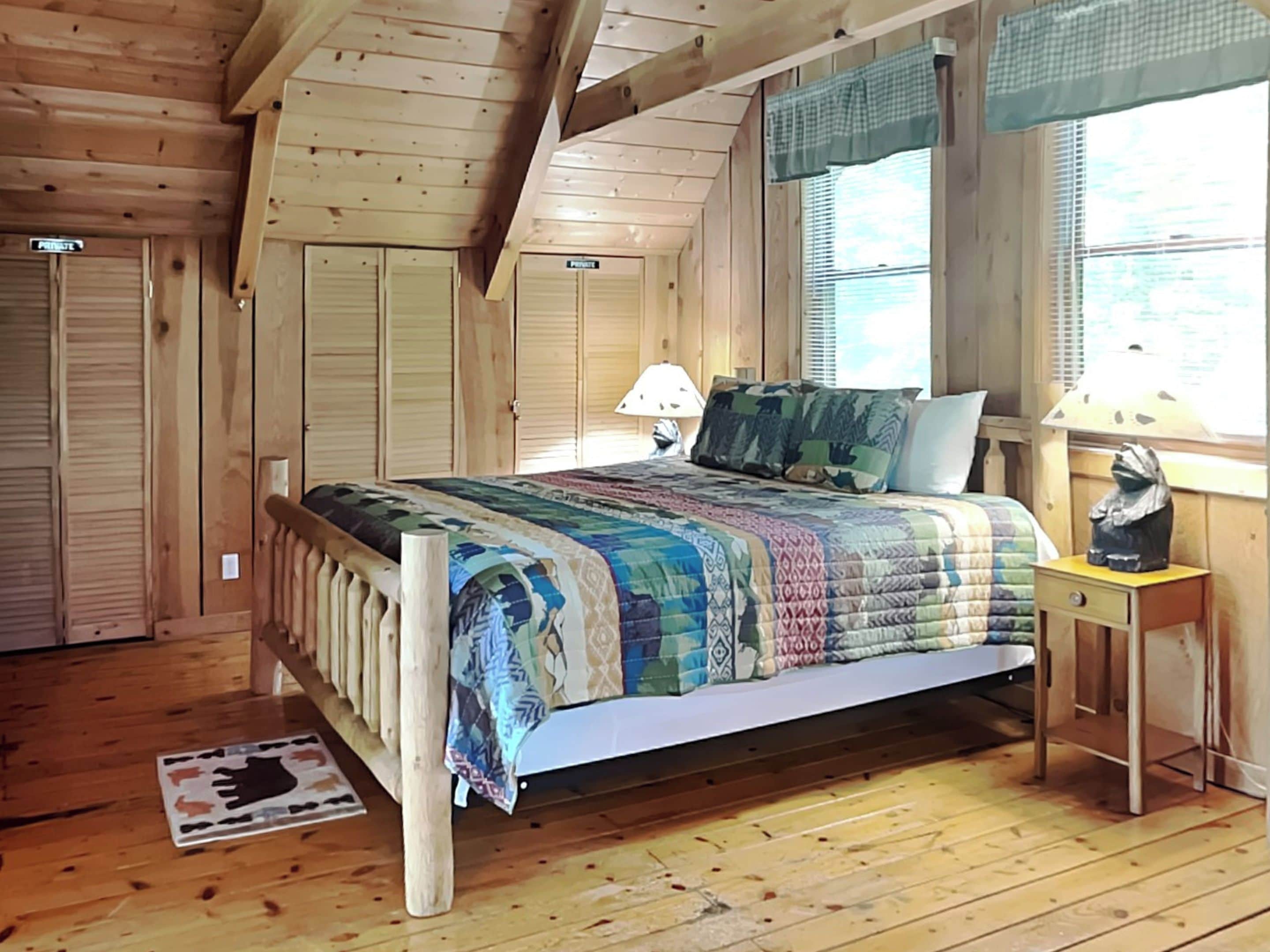 A wooden bedroom with a bed, a nightstand, a lamp, and a window with blinds.