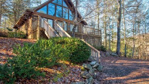 A cabin with a large glass window, wooden deck, and stairs leading to the entrance.