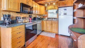 A wooden cabin kitchen with wooden cabinets, a stove, a microwave, a refrigerator, and a coffee maker.