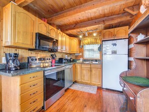 A wooden cabin kitchen with wooden cabinets, a stove, a microwave, a refrigerator, and a coffee maker.