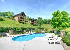 A swimming pool with lounge chairs, a stone wall, and a building with multiple balconies in the background. - A Mountain Paradise by Jackson Mountain Rentals (Sevierville)