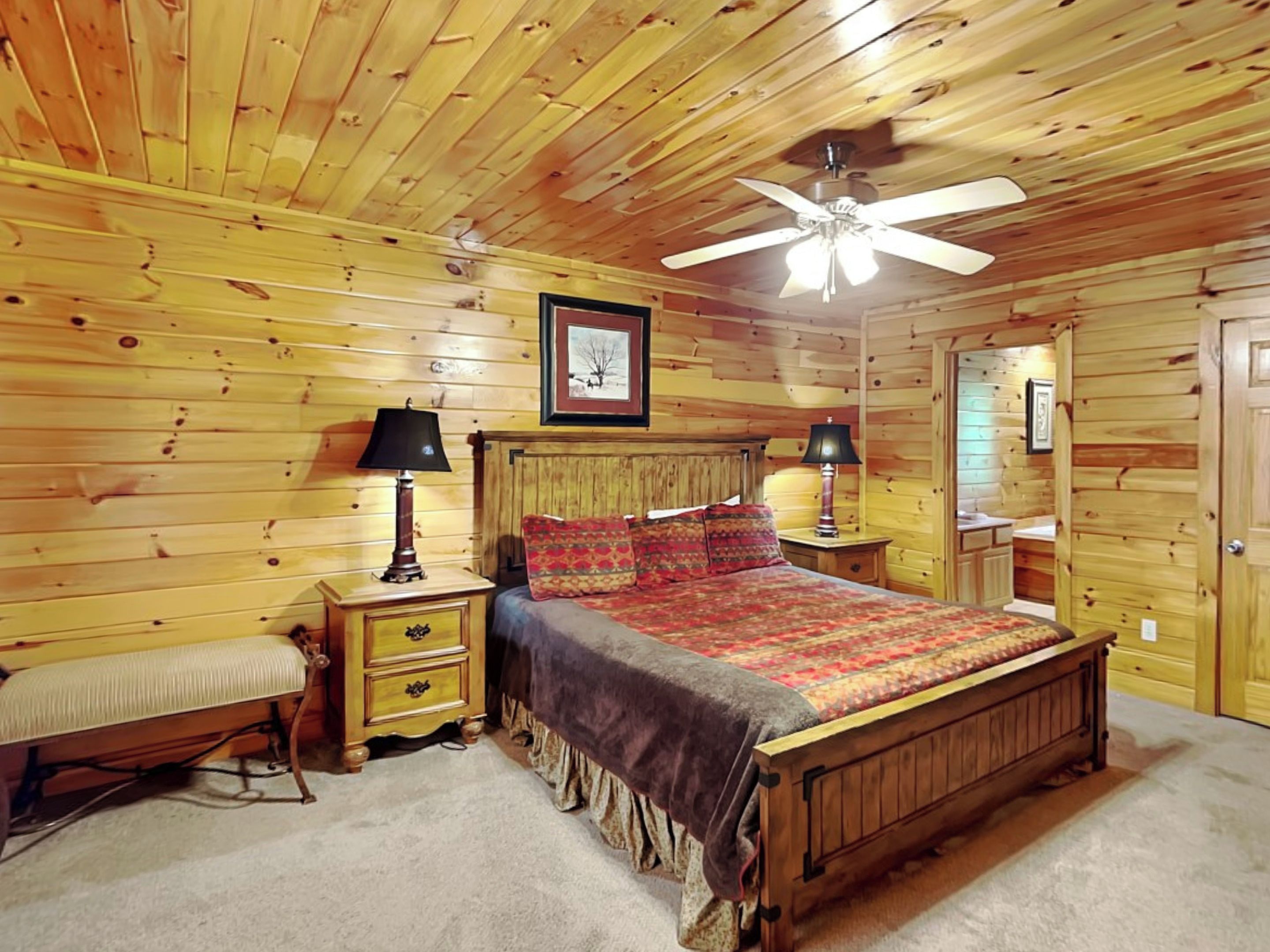 A wooden cabin bedroom with a bed, two bedside tables with lamps, a bench, and a ceiling fan.