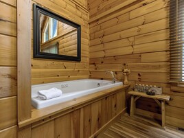 A wooden cabin bathroom with a large bathtub, a mirror, and a wooden bench with candles.