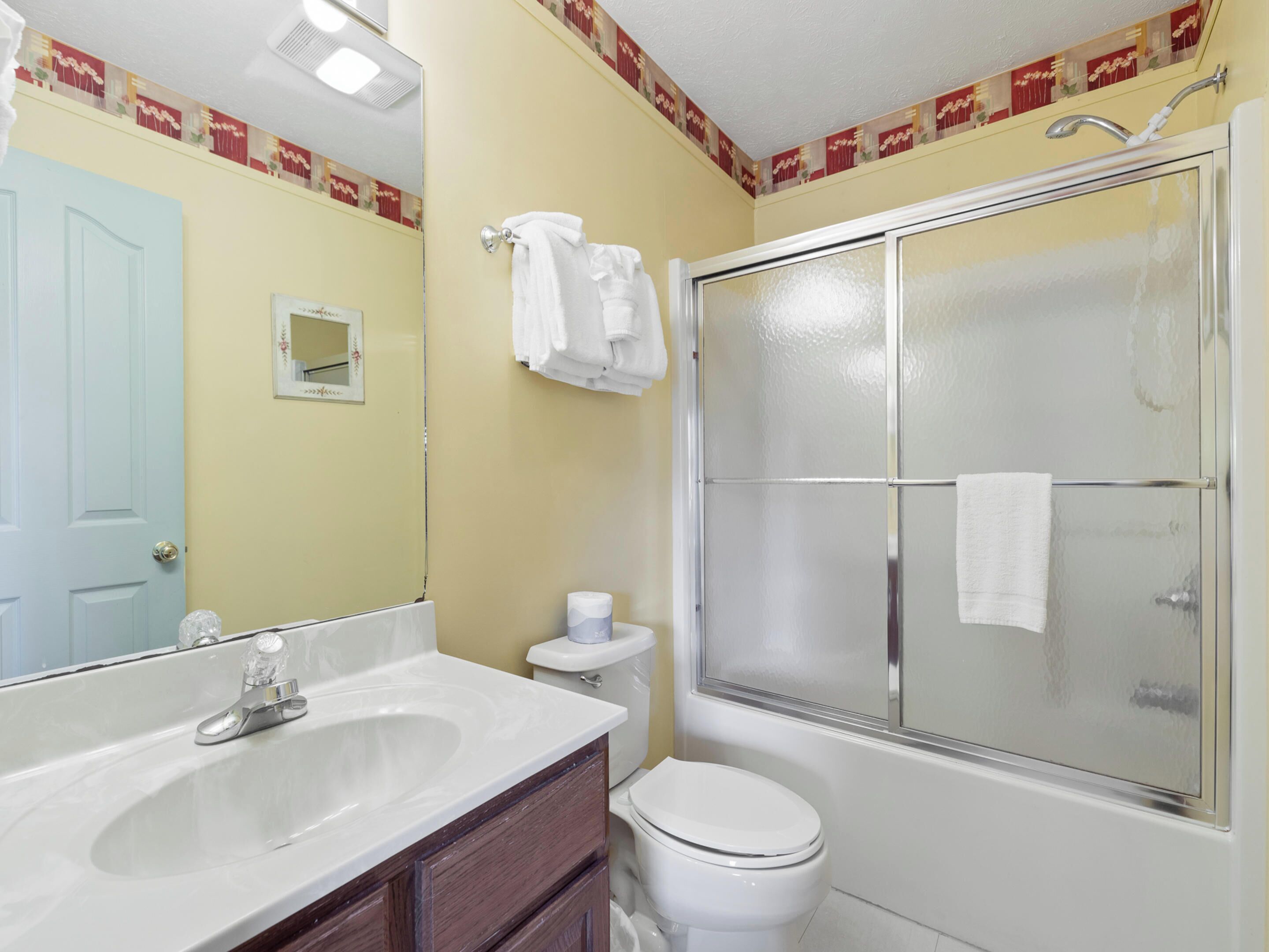 Une salle de bain avec un lavabo blanc, des toilettes et une douche fermée par une paroi de verre.