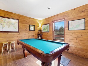 Una mesa de billar en una habitación con paredes de madera y ventanas amplias.