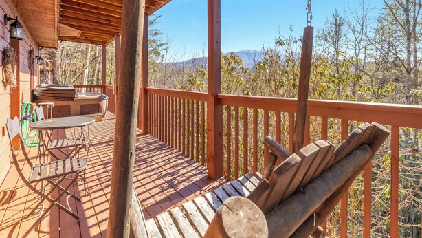 A wooden deck with a hanging swing, a barbecue area, and a view of the surrounding landscape. - Annie's Smoky View by Jackson Mountain Rentals (Gatlinburg)