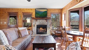 A cozy cabin interior with a stone fireplace, wooden furniture, and a television mounted above it. - Annie's Smoky View by Jackson Mountain Rentals (Gatlinburg)