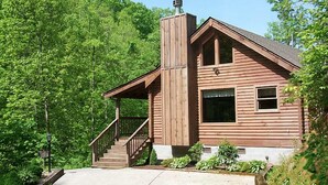 Une cabane en bois avec une cheminée, une véranda et un escalier menant à l’entrée.