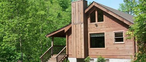 A wooden cabin with a chimney, a porch, and a staircase leading to the entrance.