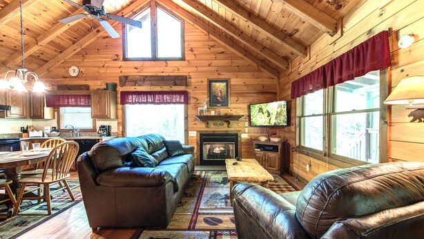 Un intérieur de chalet chaleureux avec une cheminée, des canapés en cuir, des planchers en bois et un coin repas.