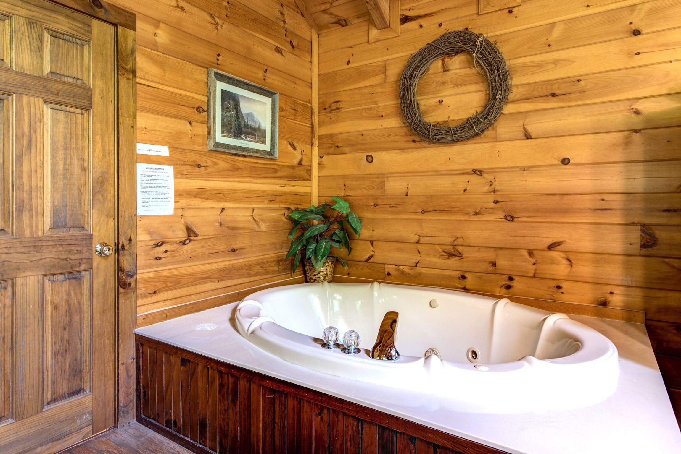 L’intérieur d’un chalet en bois, avec une grande baignoire, des murs en bois, une porte, un tableau encadré et une guirlande.