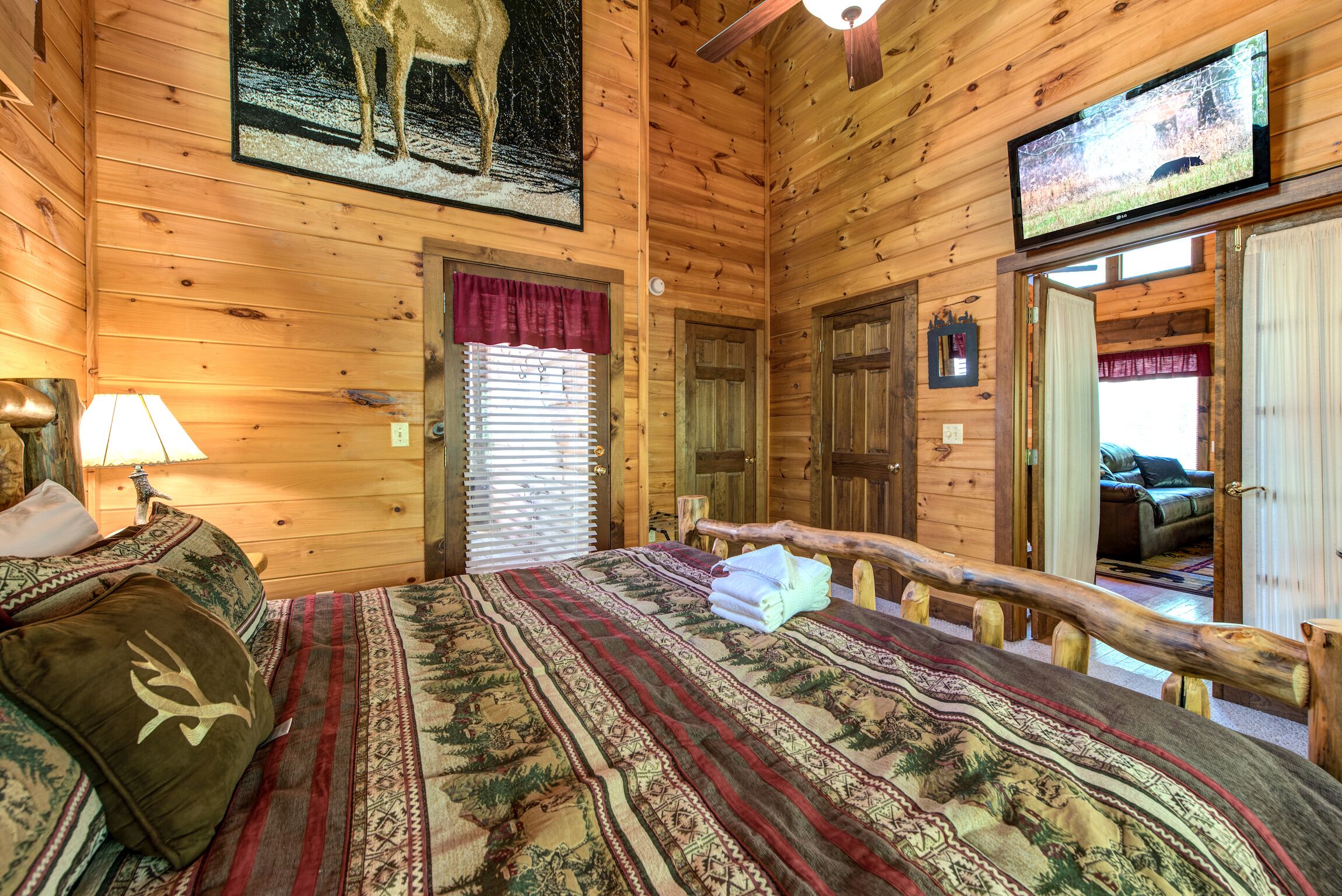 A wooden cabin room with a bed, a television, and a window with blinds.