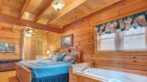 A wooden cabin bedroom with a bed, a large window with blinds, a wooden ceiling, and a wall-mounted lamp. - Dew South by Jackson Mountain Rentals (Gatlinburg)