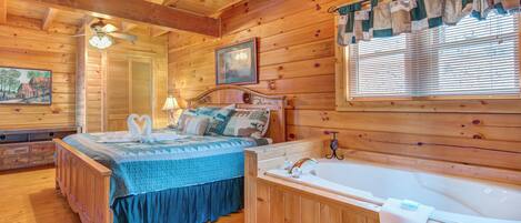 A wooden cabin bedroom with a bed, a large window with blinds, a wooden ceiling, and a wall-mounted lamp.