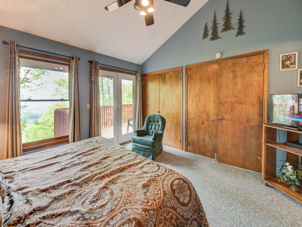 A bedroom with a large bed, a ceiling fan, a TV, and a sliding door leading to a balcony.