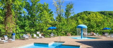 An outdoor swimming pool with lounge chairs and umbrellas, surrounded by trees.
