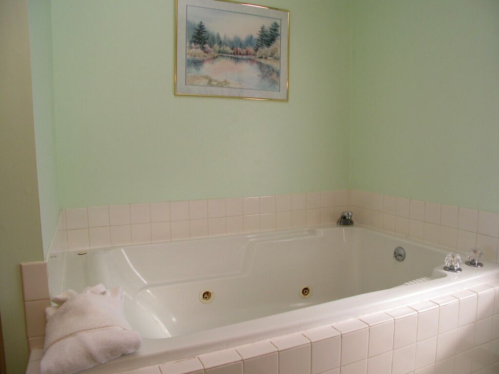 Een badkamer met een groot bad, een lijst met een foto aan de muur, en een handdoek op de rand.