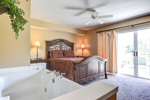 Un dormitorio con una cama grande, ventilador de techo, bañera y vistas al exterior a través de un ventanal corredero.