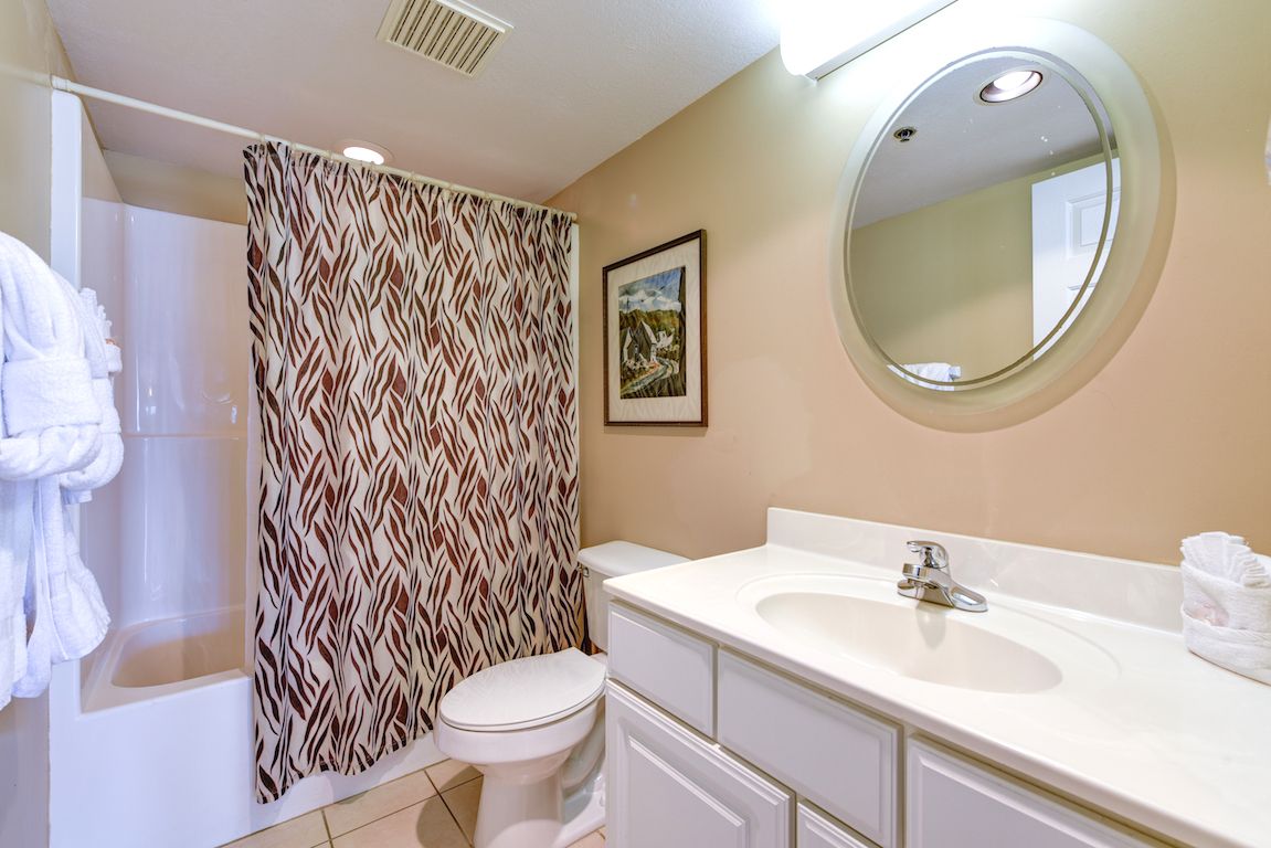 A bathroom with a shower, toilet, sink, and a mirror.