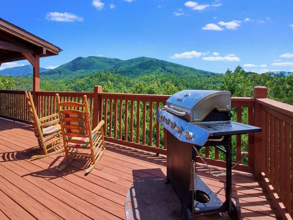 A wooden deck with a barbecue grill and a rocking chair, overlooking a mountainous landscape.