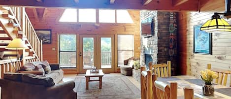A spacious living area with a wooden floor, a sofa, a dining table with chairs, a fireplace, and a staircase leading to another level.
