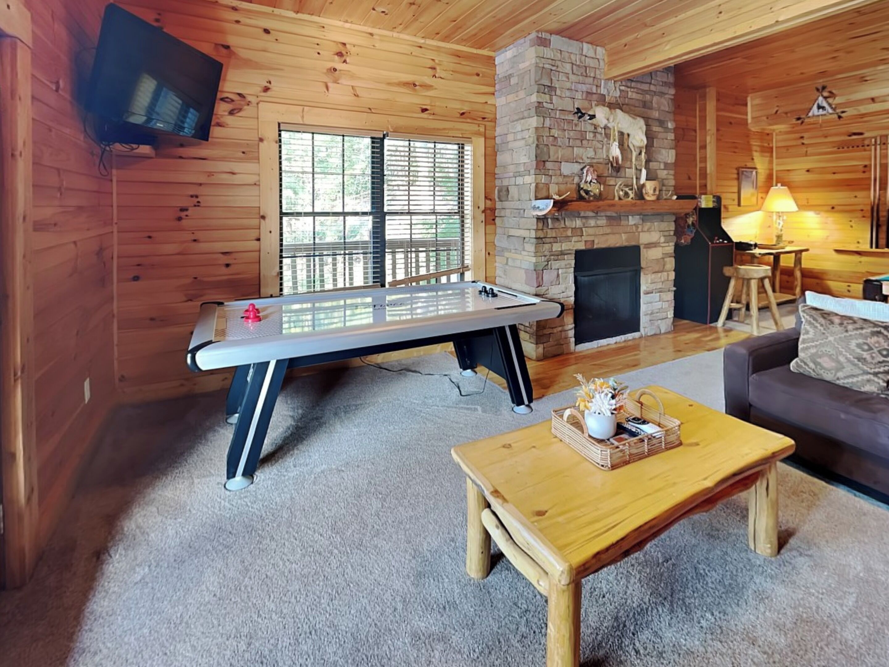 A cozy room with a foosball table, a fireplace, a sofa, and a television mounted on the wall.