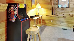 A wooden cabin interior with a Multicade arcade machine, a small table with a lamp, and a wooden stool. - A Majestic View III by Jackson Mountain Rentals (Townsend)